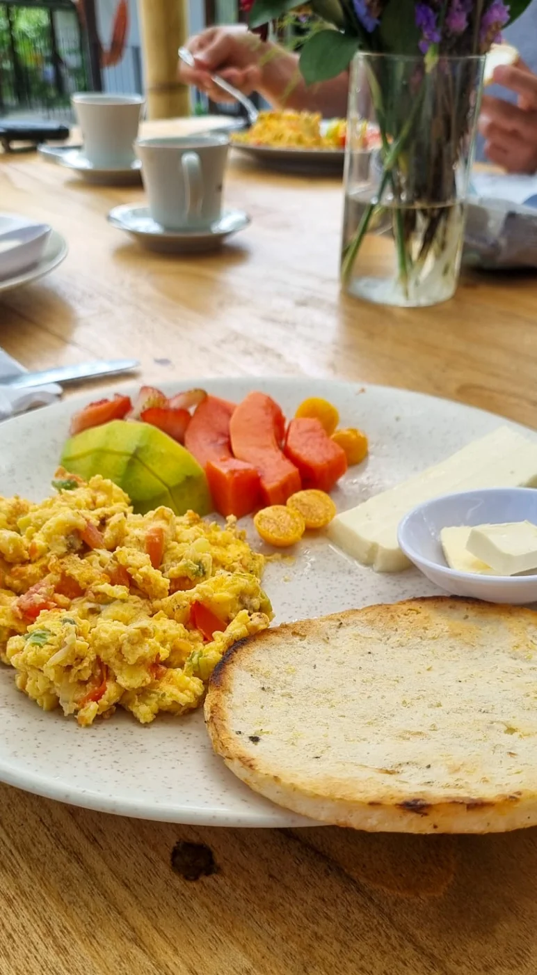 Desayuno con huevos revueltos, arepa, fruta y café